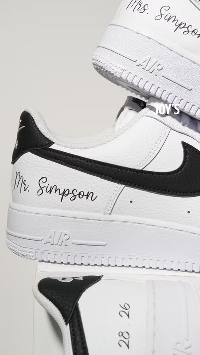 White custom Nike Air Force 1 sneakers with black swoosh, personalized last name and wedding date printed on the side, shown in a clean close-up view