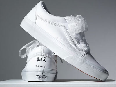 Custom white Vans sneakers with pearl trim and “Mrs.” lettering on the heel, designed as bridal shoes.