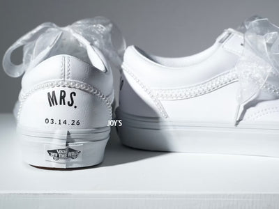 Custom white Vans sneakers with pearl trim and “Mrs.” lettering on the heel, designed as bridal shoes.