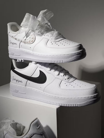 White custom wedding sneakers with pearl and rhinestone embellished swoosh, satin ribbon laces, and personalized last name printed on the side, shown in a close-up detail view