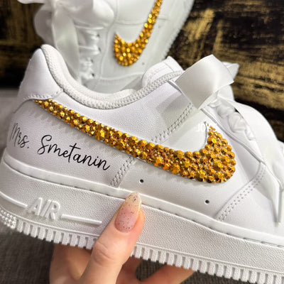White custom wedding sneakers featuring gold rhinestone swooshes, personalized name and wedding date on the heel, shown in a close-up detail view