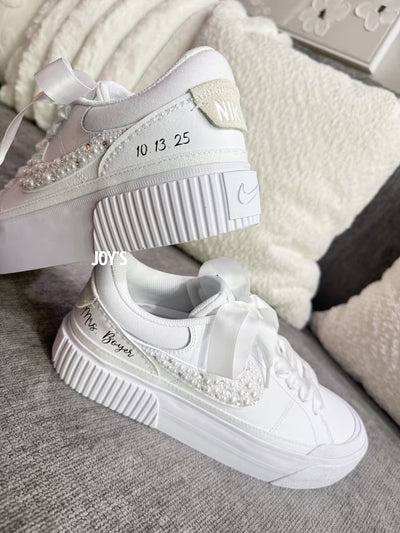 White custom wedding sneakers with pearl and rhinestone embellished swoosh, satin ribbon laces, and personalized bride name and wedding date on the heel