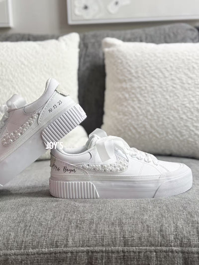 White custom wedding sneakers with pearl and rhinestone embellished swoosh, satin ribbon laces, and personalized bride name and wedding date on the heel