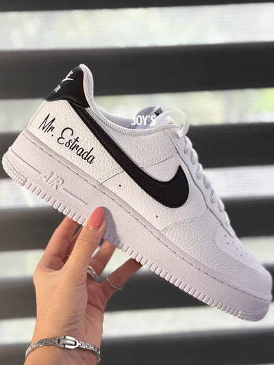 White custom Nike Air Force 1 sneakers with black swoosh, personalized last name and wedding date printed on the side, shown in a clean close-up view