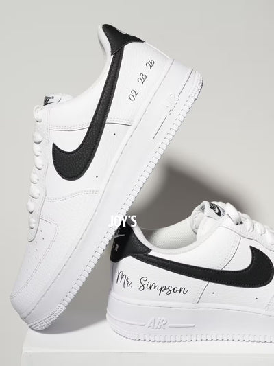 White custom Nike Air Force 1 sneakers with black swoosh, personalized last name and wedding date printed on the side, shown in a clean close-up view