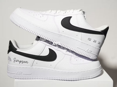 White custom Nike Air Force 1 sneakers with black swoosh, personalized last name and wedding date printed on the side, shown in a clean close-up view