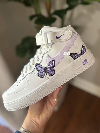 Custom white Nike Air Force 1 Mid Sneakers with hand-painted purple butterfly artwork and soft lilac swoosh.