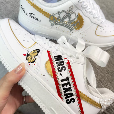 White custom wedding sneakers with pearl-embellished heel, rhinestone details, red and blue painted accents, and personalized “Mrs. Texas” text on the side, shown in a close-up side view