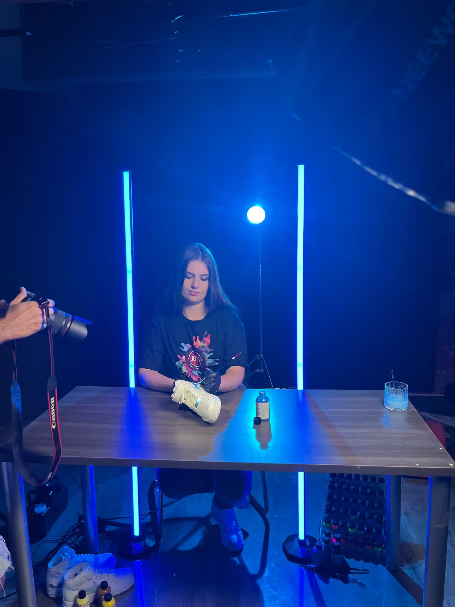 Artist Joy Perez is sitting at a table with blue lights and equipment in a studio setting