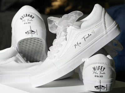 White custom wedding sneakers with pearl trim and personalized bride and groom names, wedding date, and “Wifey” and “Husband” heel text shown in a close-up detail view