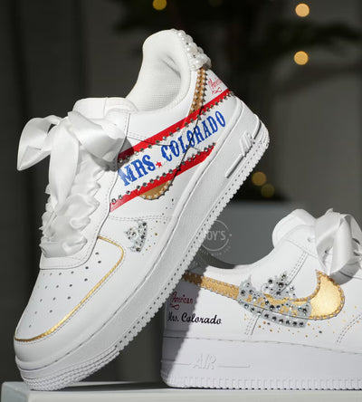 White custom wedding sneakers with pearl-embellished heel, rhinestone details, red and blue painted accents, and personalized “Mrs. Colorado” text on the side, shown in a close-up side view
