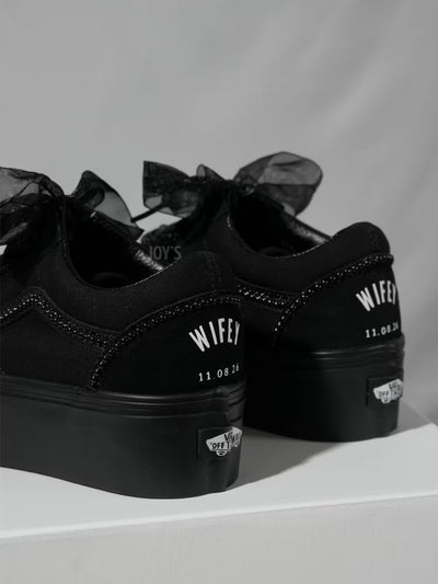 Black platform Vans custom wedding sneakers with pearl trim, satin ribbon laces, and “Wifey” text with wedding date printed on the heel, shown in a close-up rear view