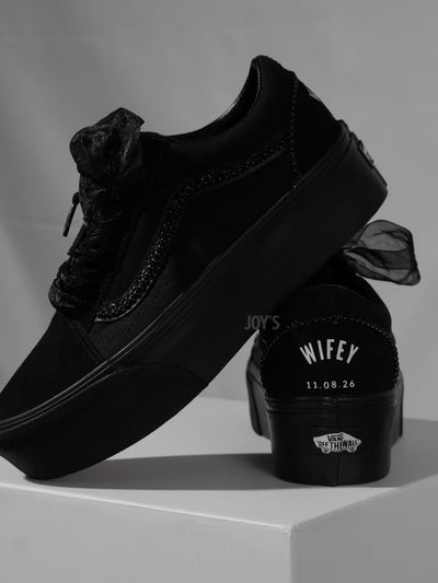 Black platform Vans custom wedding sneakers with pearl trim, satin ribbon laces, and “Wifey” text with wedding date printed on the heel, shown in a close-up rear view
