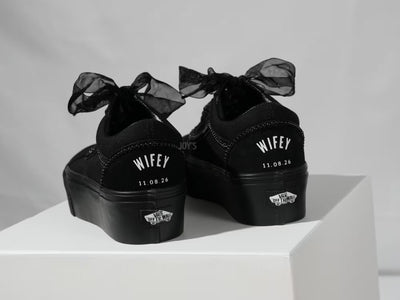 Black platform Vans custom wedding sneakers with pearl trim, satin ribbon laces, and “Wifey” text with wedding date printed on the heel, shown in a close-up rear view