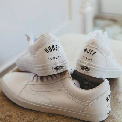 Custom white Vans platform sneakers with “Hubby” and “Wifey” lettering and wedding date printed on the heels, designed as matching bridal shoes.