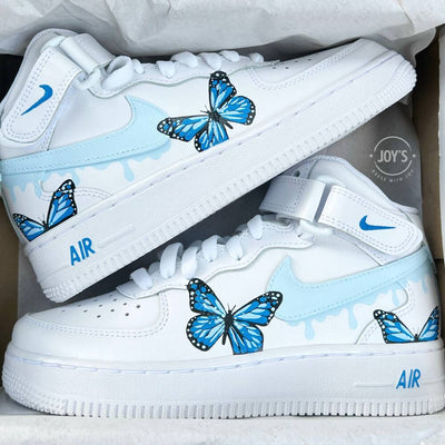 White Nike Air Force 1 Mid Sneakers with light blue drip swoosh and hand-painted blue butterfly design.