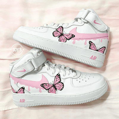 Pair of custom white Nike Air Force 1 sneakers with pink drip swoosh and hand-painted pink butterfly designs, displayed side by side on a soft pink background.
