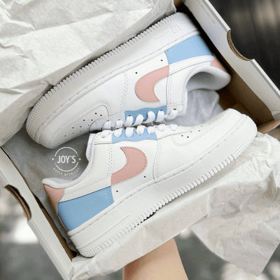 Pair of custom white Nike Air Force 1 sneakers in a shoebox, featuring pastel color-block swooshes in light blue and peach.