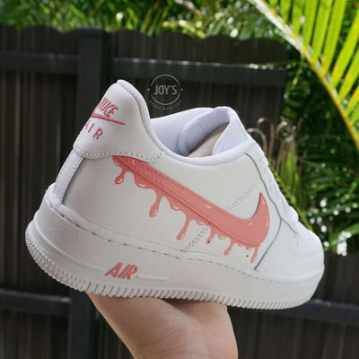 White Nike Air Force 1 sneakers with coral pink dripping swoosh design 