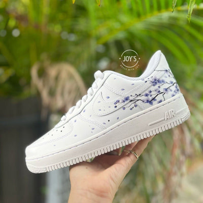 Custom white Nike Air Force 1 with purple cherry blossom splatter details shown at an angle